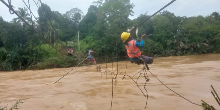 Petugas PLN saat membenahi jaringan kabel listrik yang terhantam banjir di atas jembatan gantung. (DETAIL/Daryanto)